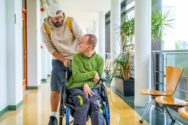 Young man pushing wheelchair of friend with disability around university campus